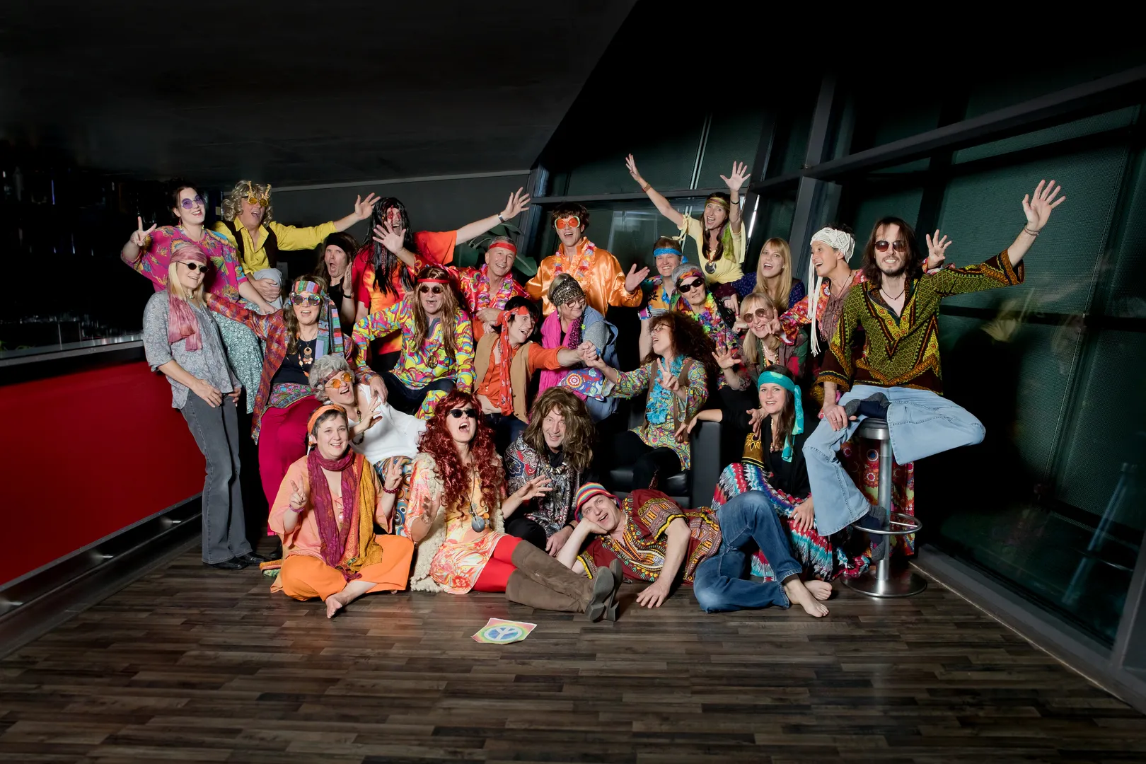 Der Chor im Hippie-Look beim Fototermin 2019: bunt gemusterte Hemden und Kleider, Stirnbänder, runde Sonnenbrillen und lange Perücken, viele lachen und reißen die Arme hoch.